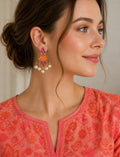 Woman wearing colorful earrings and a pink floral top against a neutral background